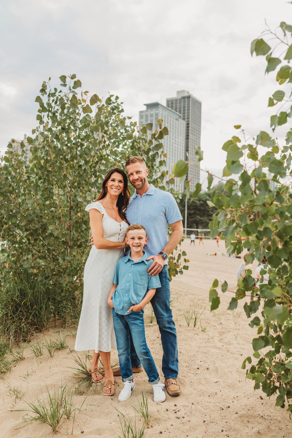 Family group stands among beach vegetation with city skyline in distance.