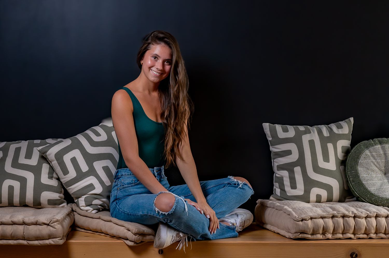 A casual indoor teen portrait with someone in jeans and green top sitting on cushions.