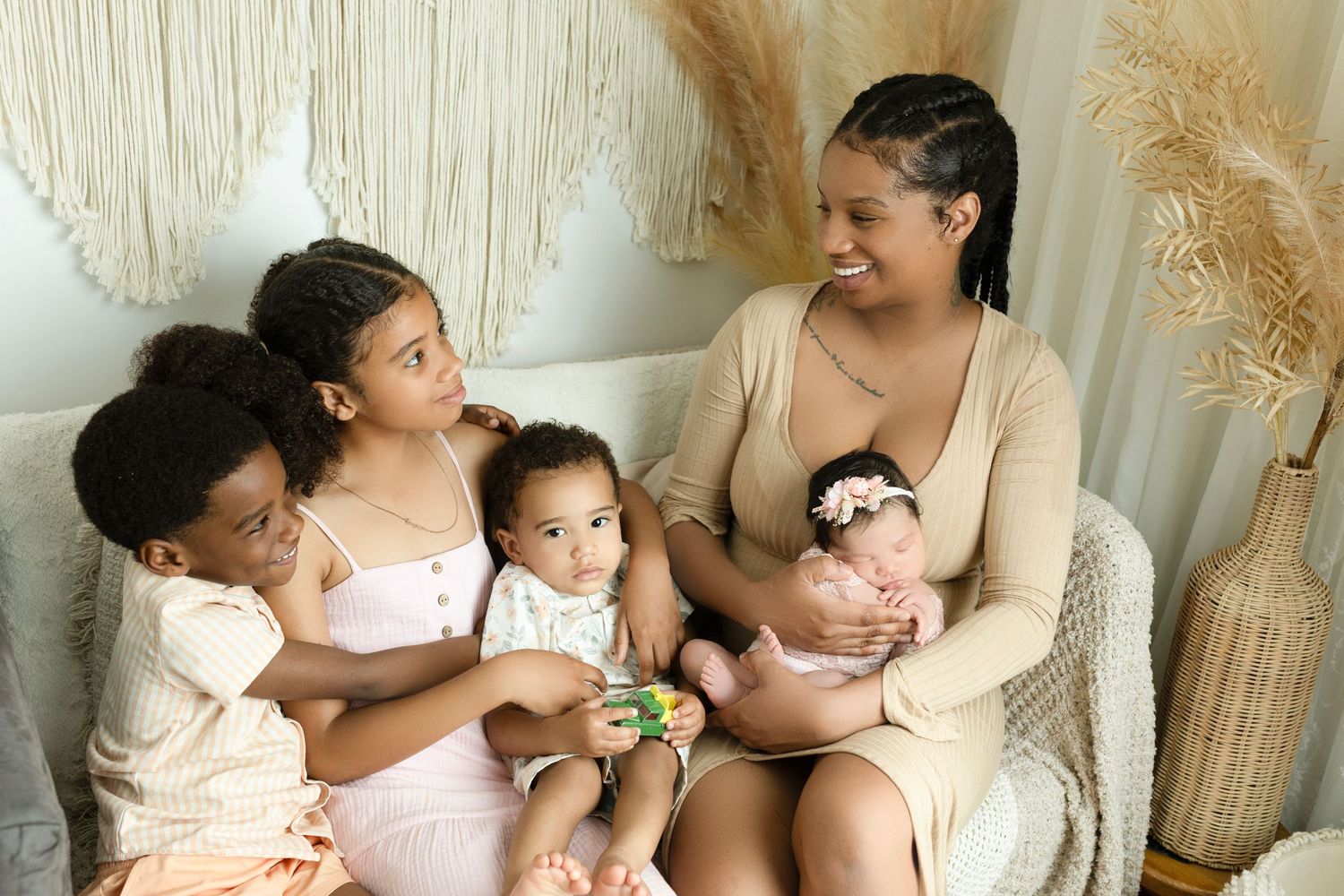 Family gathered on white wicker chair with neutral boho decor and pampas grass.