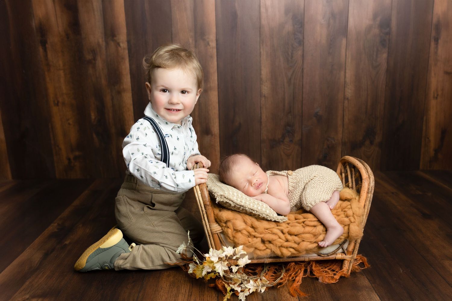 Two siblings in a rustic setting with a woven basket and dried flowers on wooden floor.