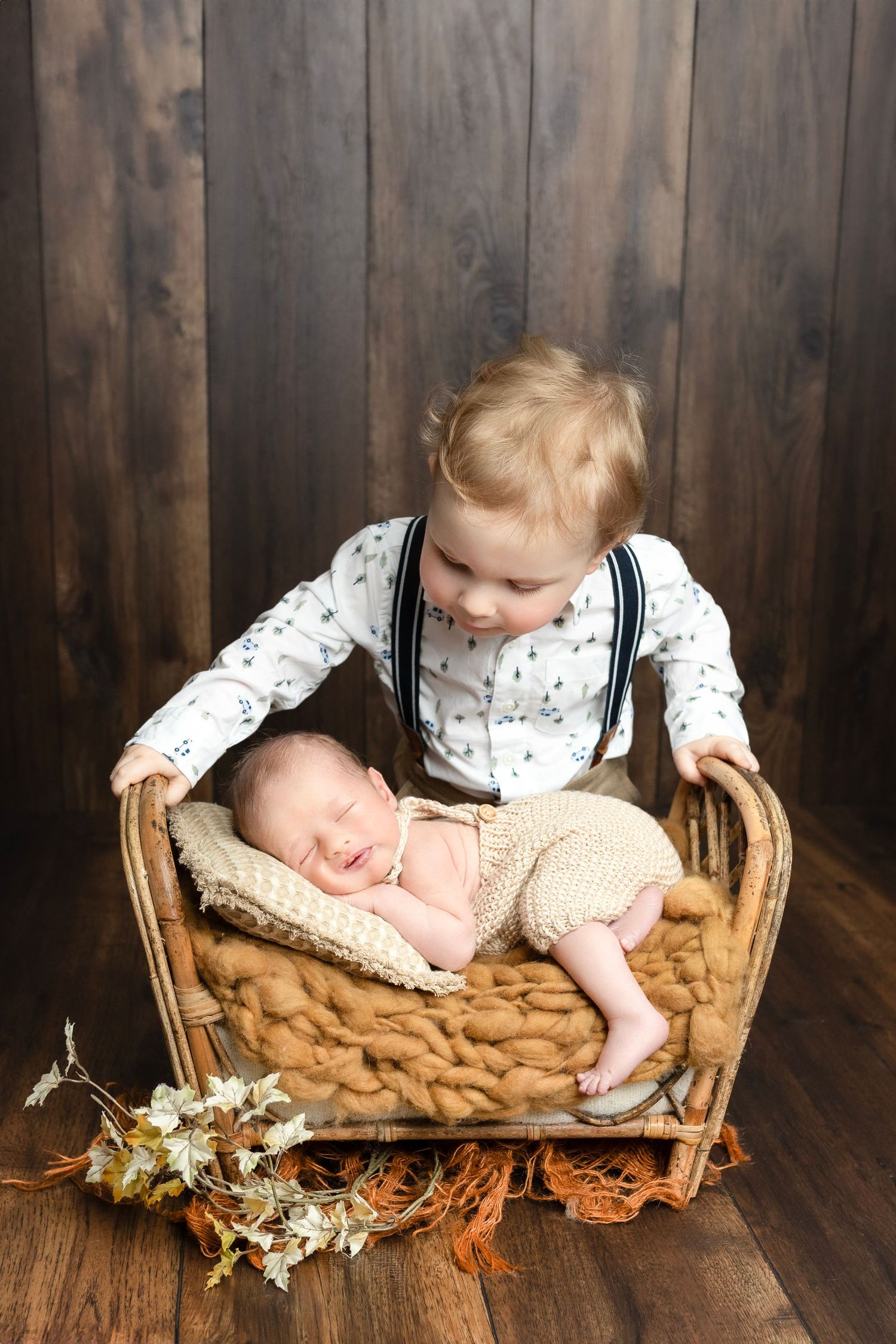 Siblings share a sweet moment near a woven basket with dried flowers on wooden floor.