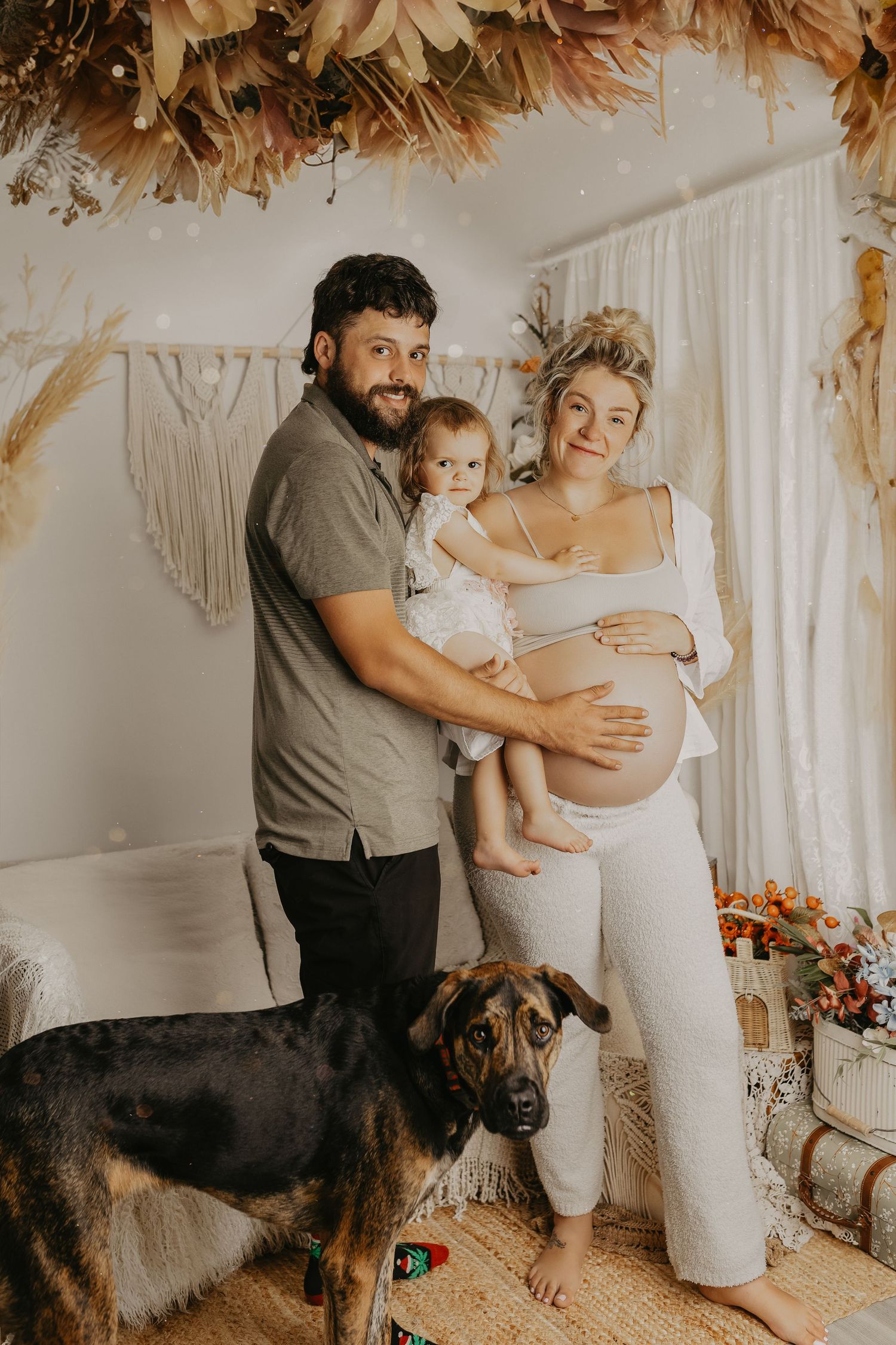 Family maternity session with dog in boho-inspired setting with dried pampas grass decor.