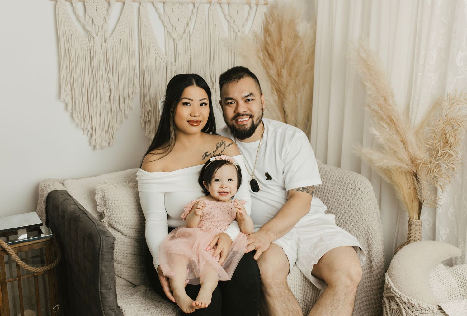 Family portrait in neutral tones with macrame wall hanging and pampas grass decor.