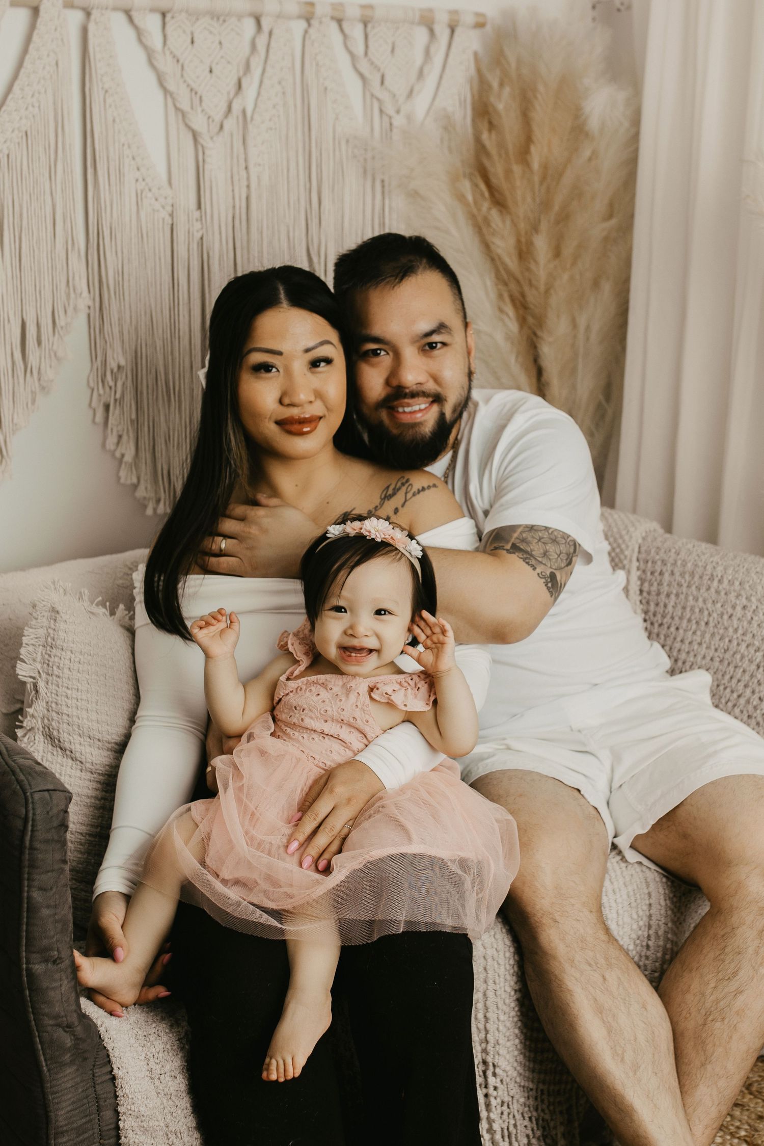 Cozy family portrait on grey couch with macrame and boho decor in background.
