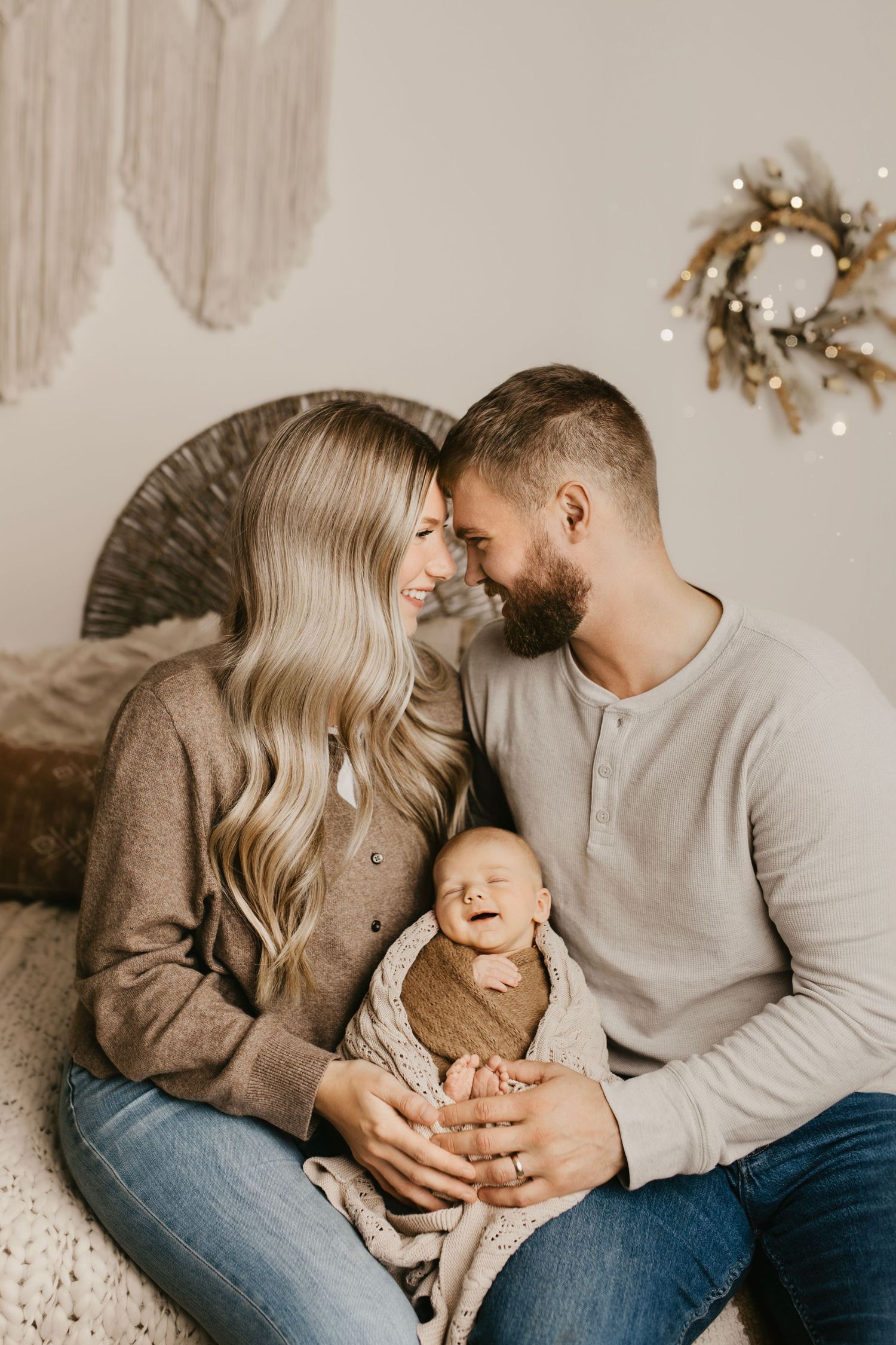 A tender family moment captured in warm tones as parents share loving glances with their sleeping infant.