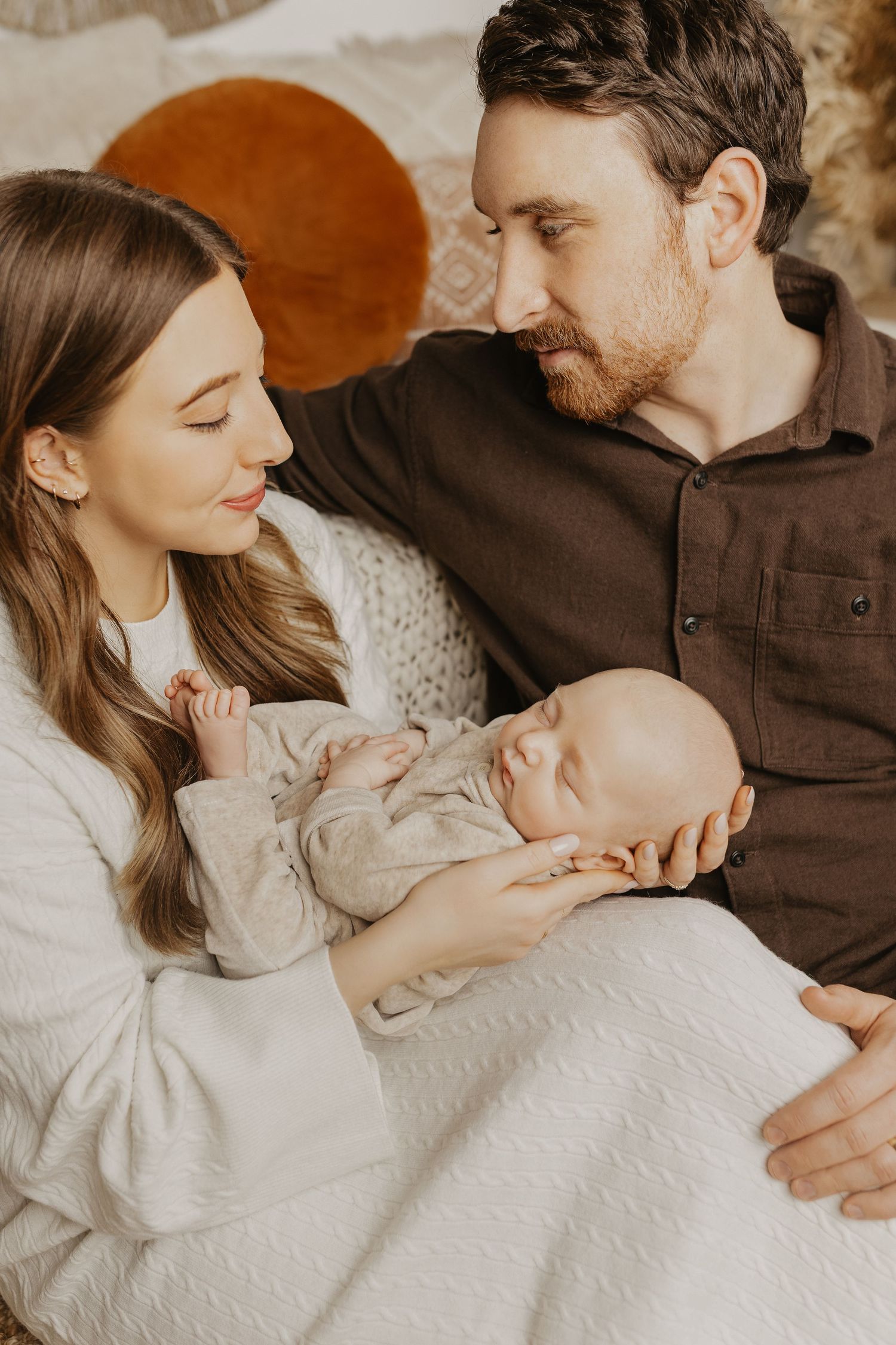 Family lying together on white textured bedding in warm natural light.