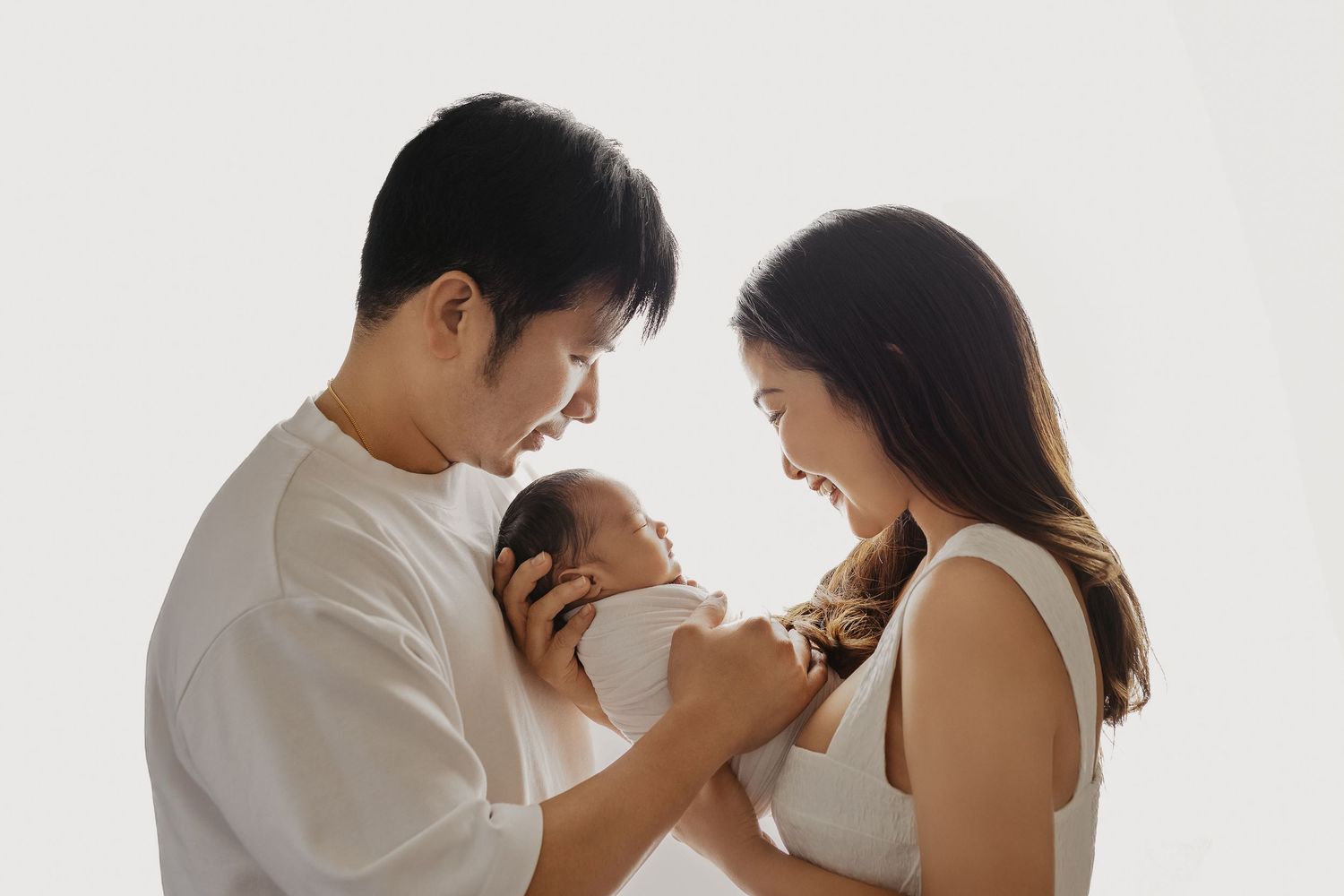 A family in white clothing poses together lovingly for intimate portraits against a light background.
