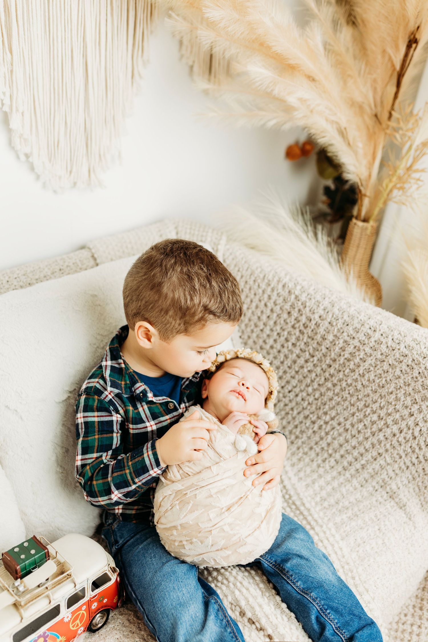 Tender moment between siblings on white couch with pampas grass decor.