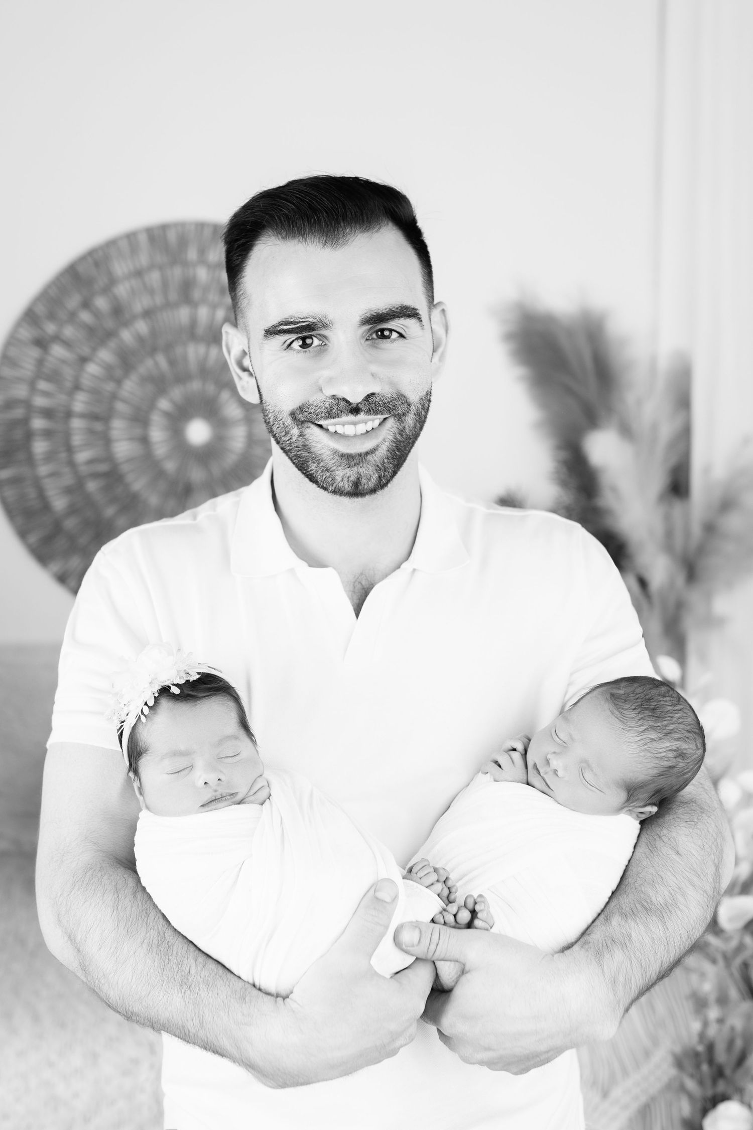 Smiling father holding twin newborn babies in black and white portrait photo.