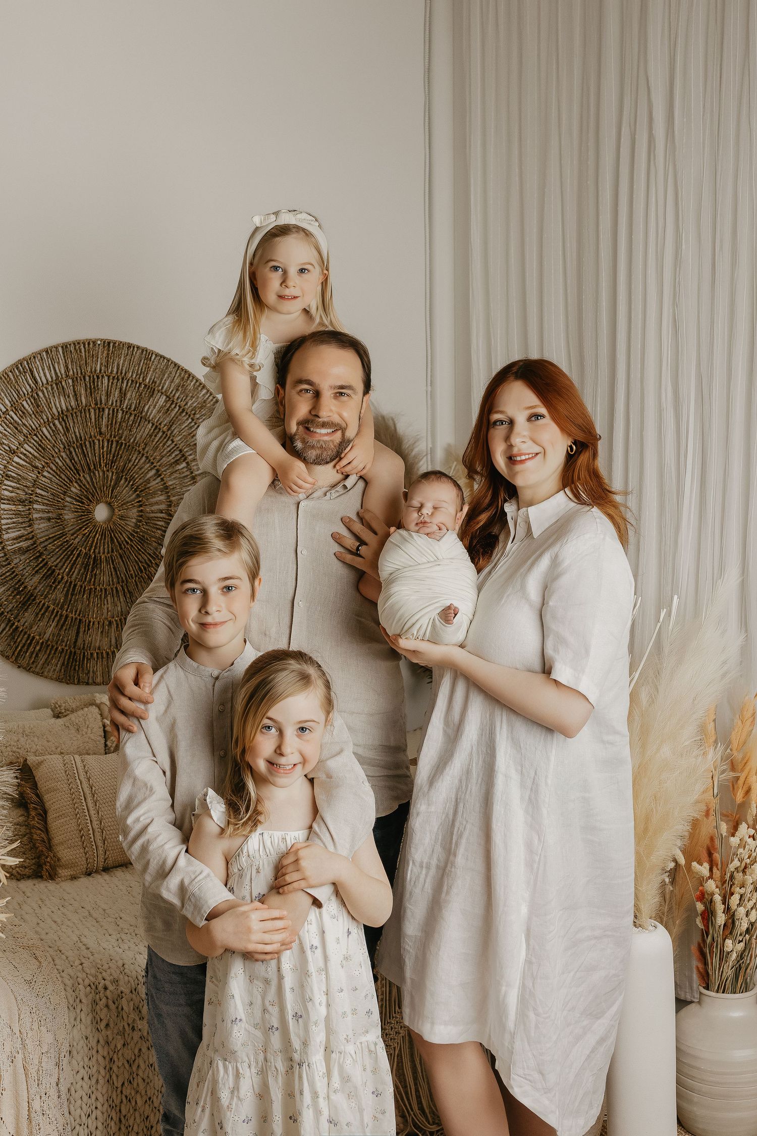Happy family of six posing together in a cozy boho-styled room, parents with four children including a newborn baby.