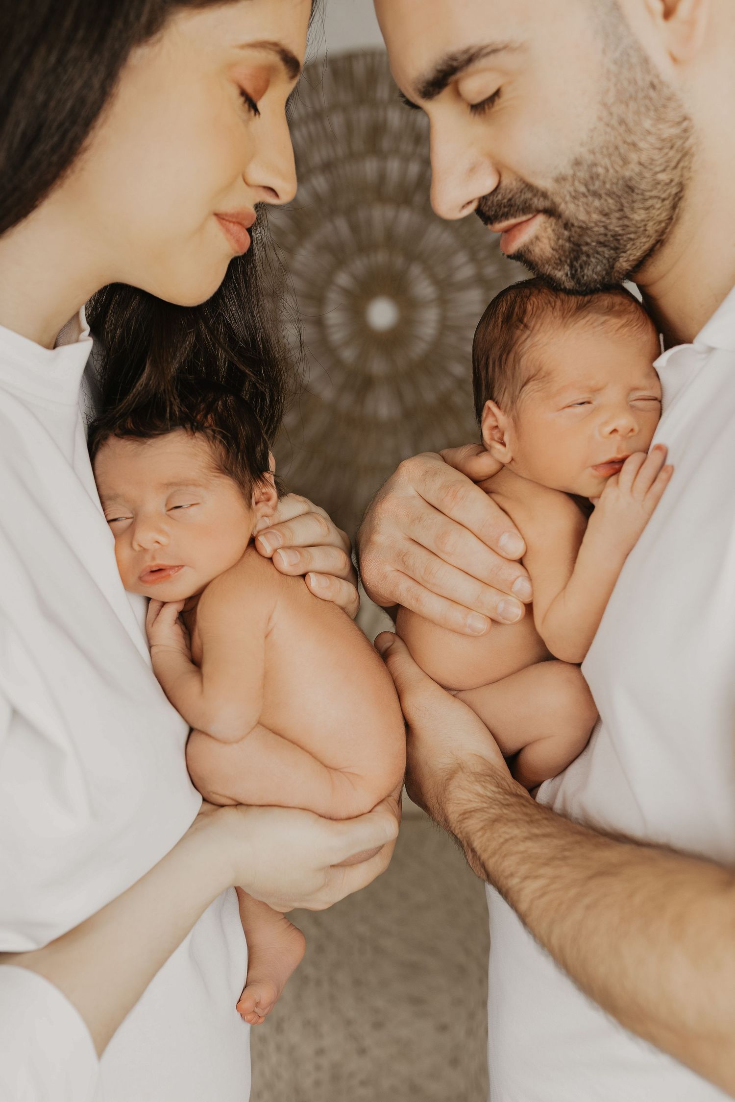 Parents tenderly holding their twin newborns face to face in a heartwarming photo.