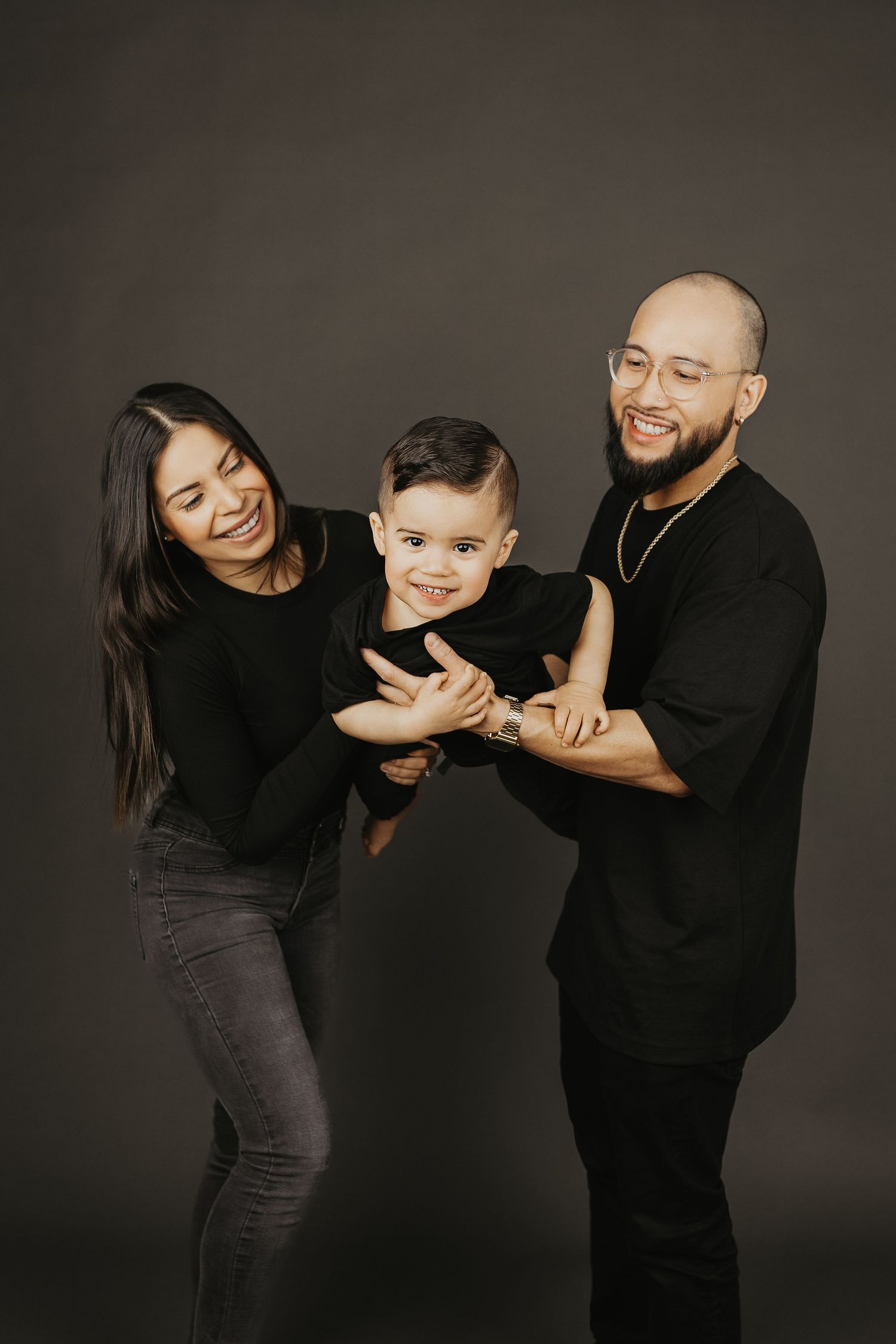Family of three in matching black outfits laughing together in a studio portrait session.