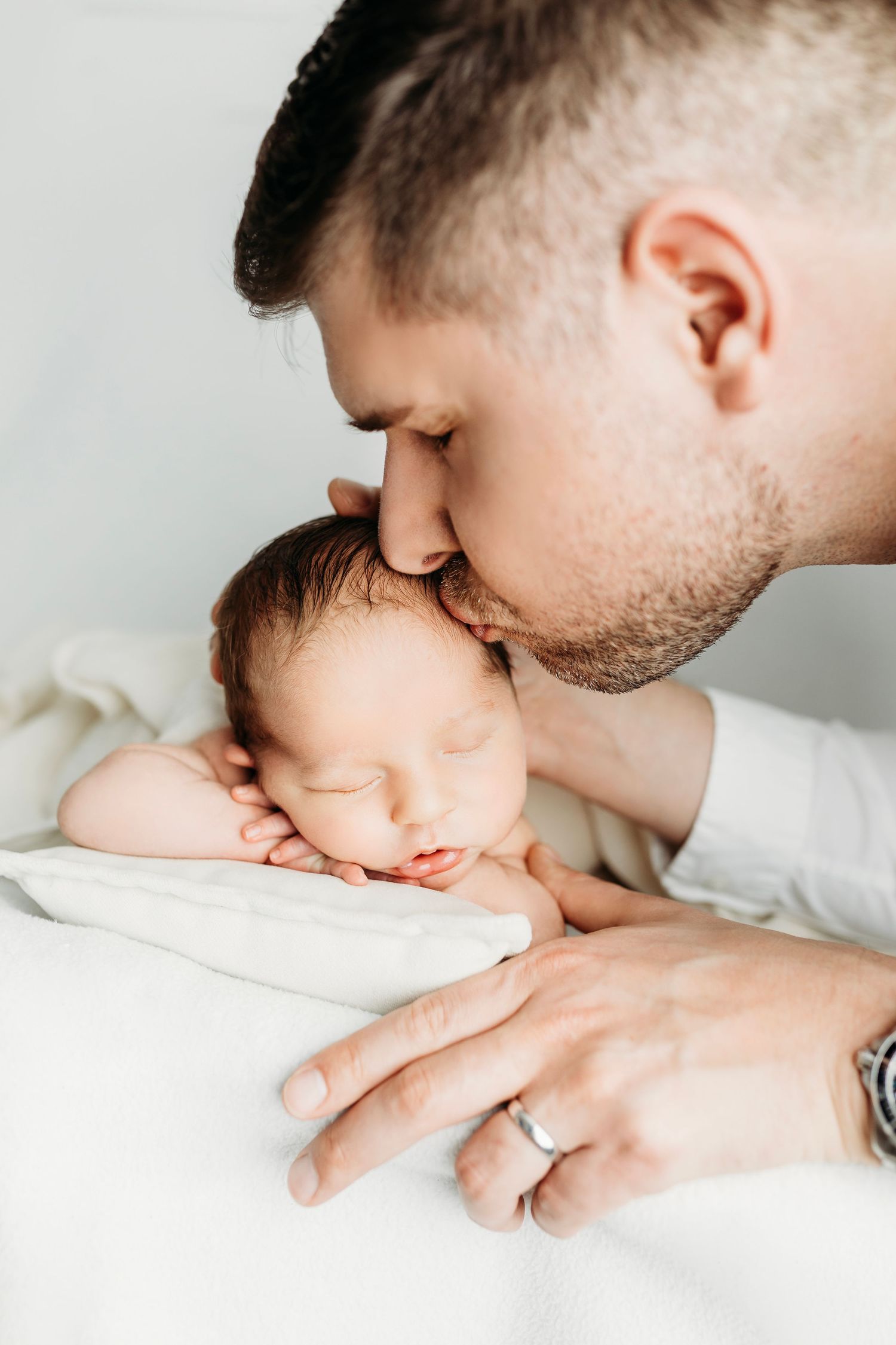 Intimate newborn photography showing gentle moments on white bedding.