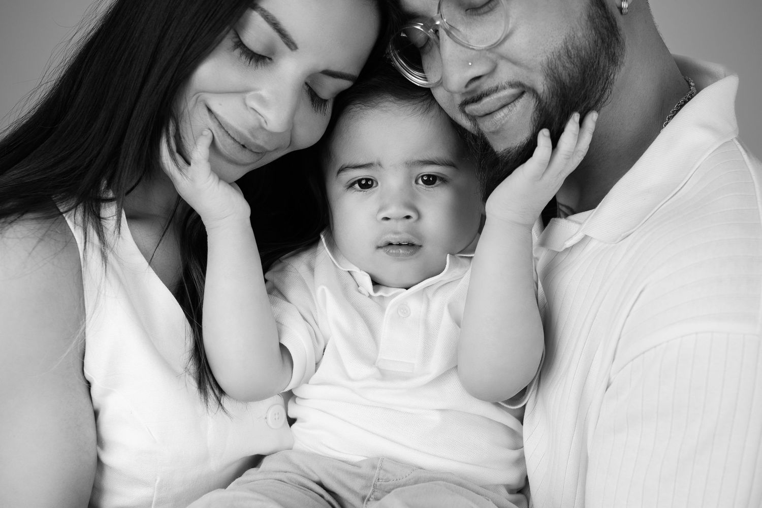 Black and white family portrait of parents lovingly cradling their baby boy in a studio setting.