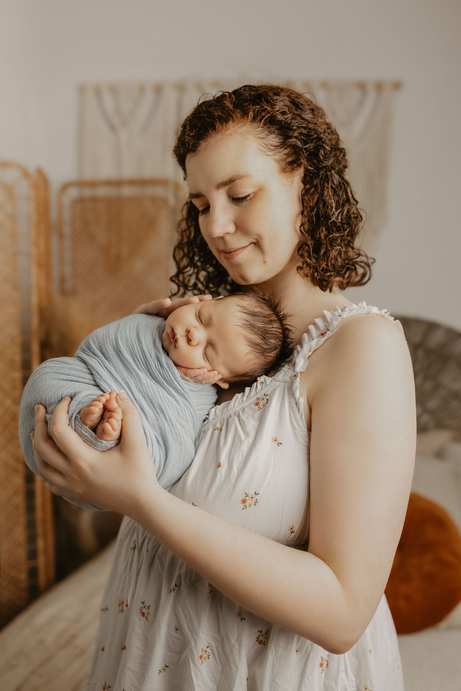 Mother in floral dress holding and bonding with sleeping newborn in natural light setting.