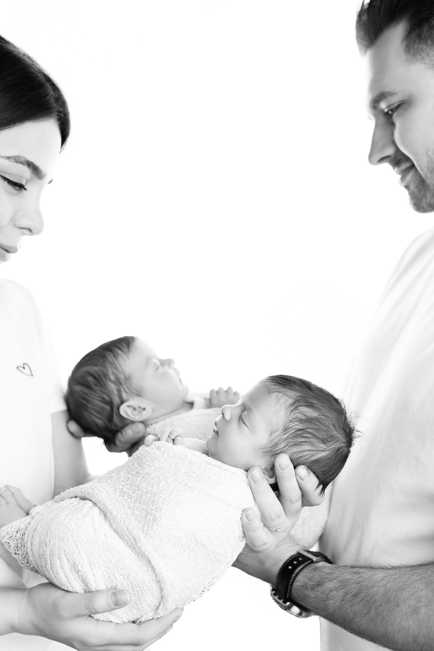 Black and white photo of parents holding their twin newborn babies against a white background.