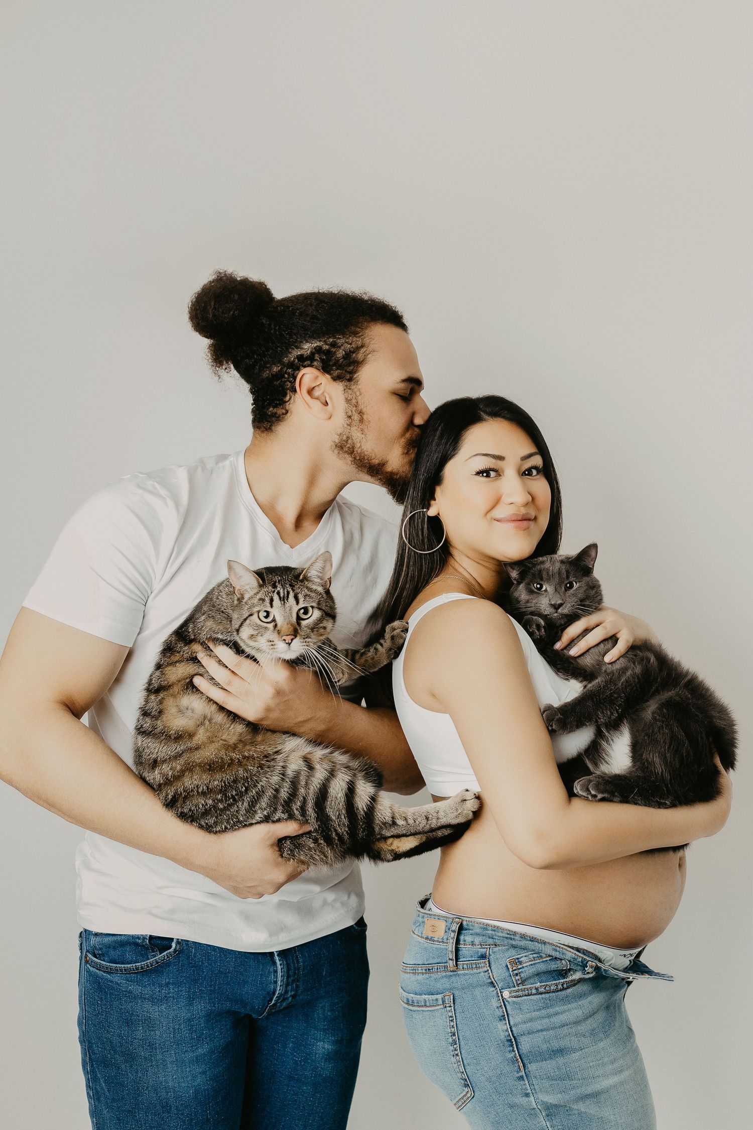 Couple holding their tabby cats while posing against neutral background.