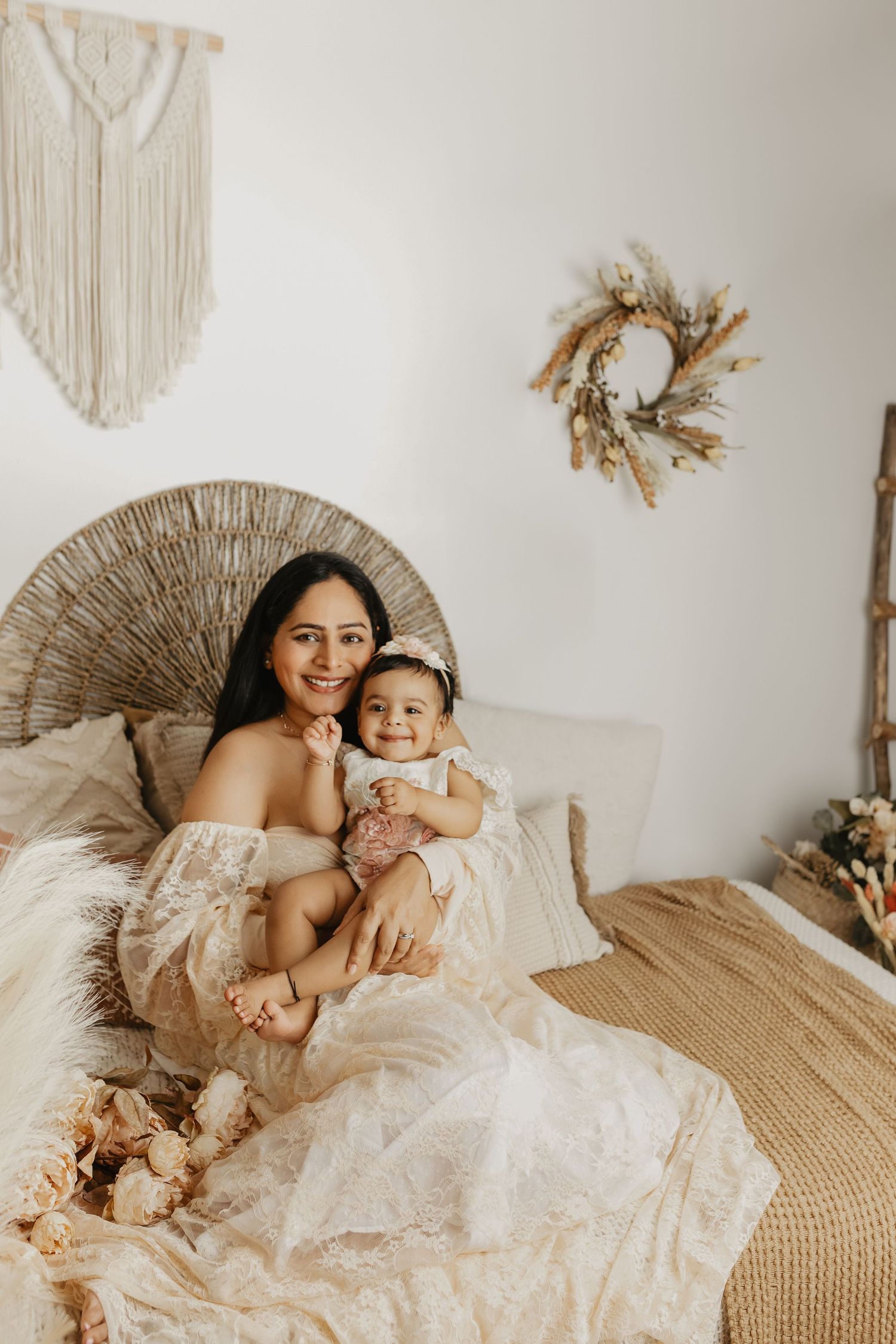 Mother and child share loving moments on a beige rattan chair against a white wall with macrame decor.