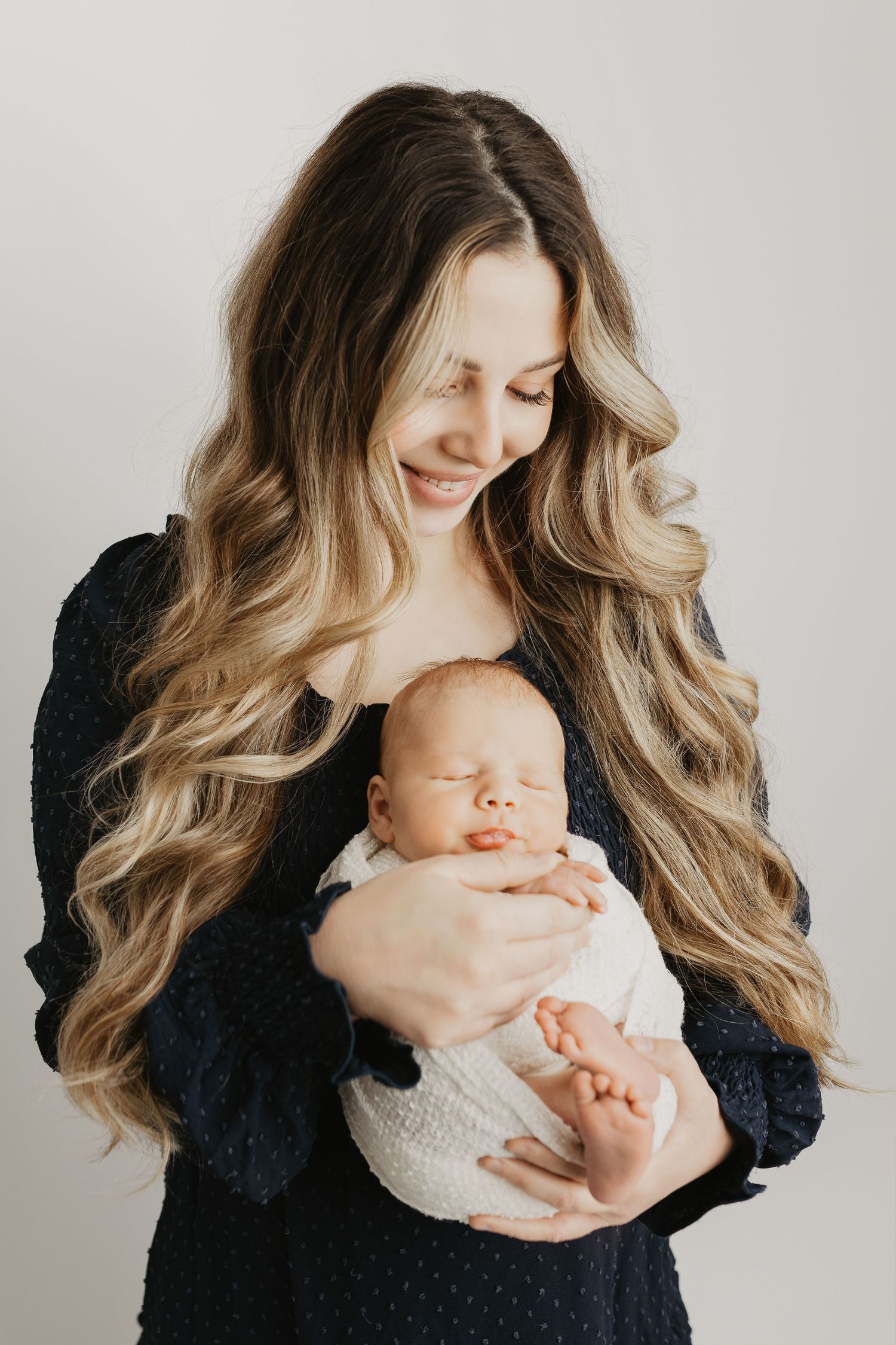 Artistic newborn portrait series with mother in navy dress against white background.