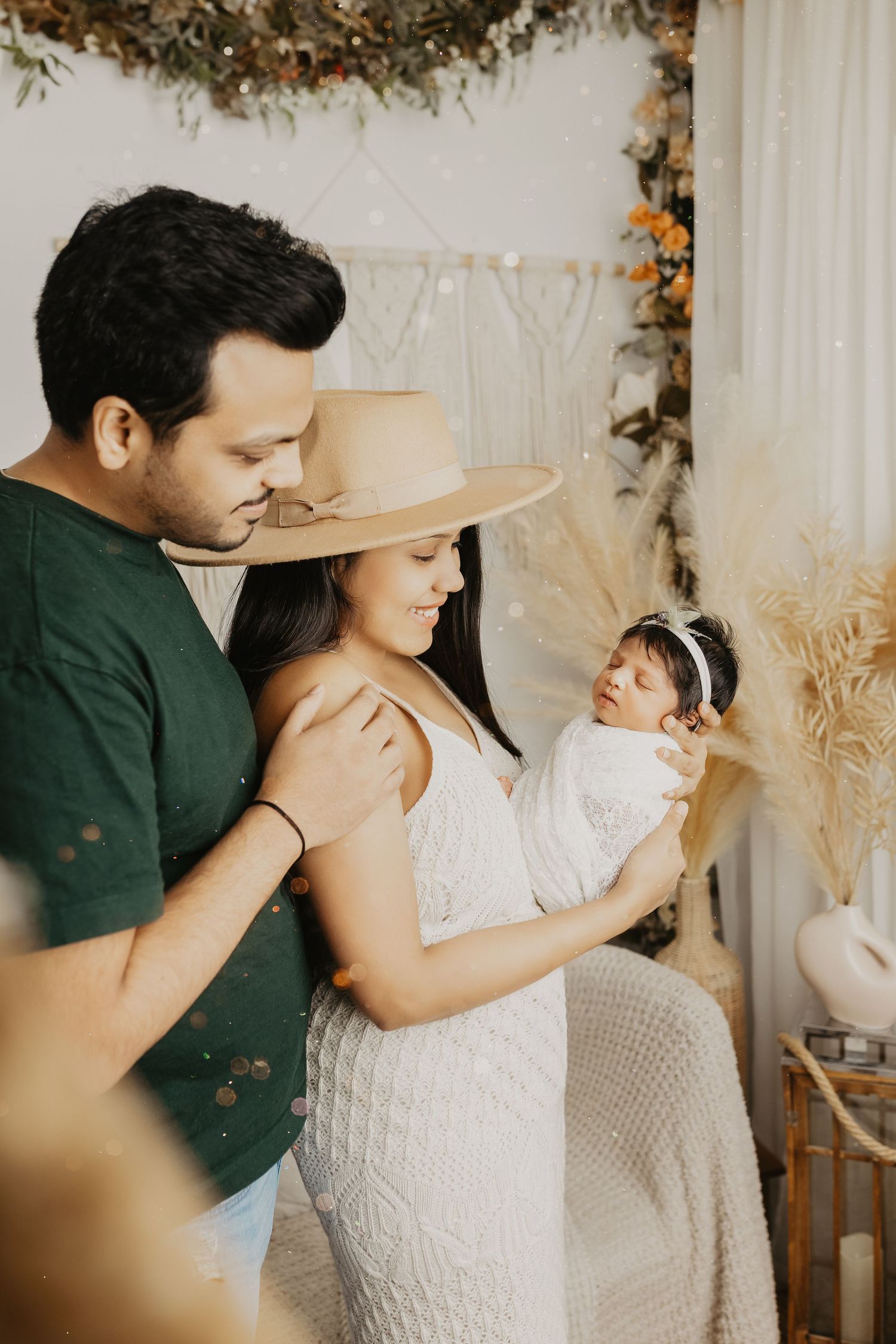 Family shares intimate moment with newborn in boho-styled room with dried flowers and hat decor.