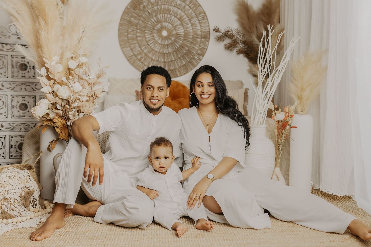 A family wearing white outfits sits together on a couch for a professional portrait session.