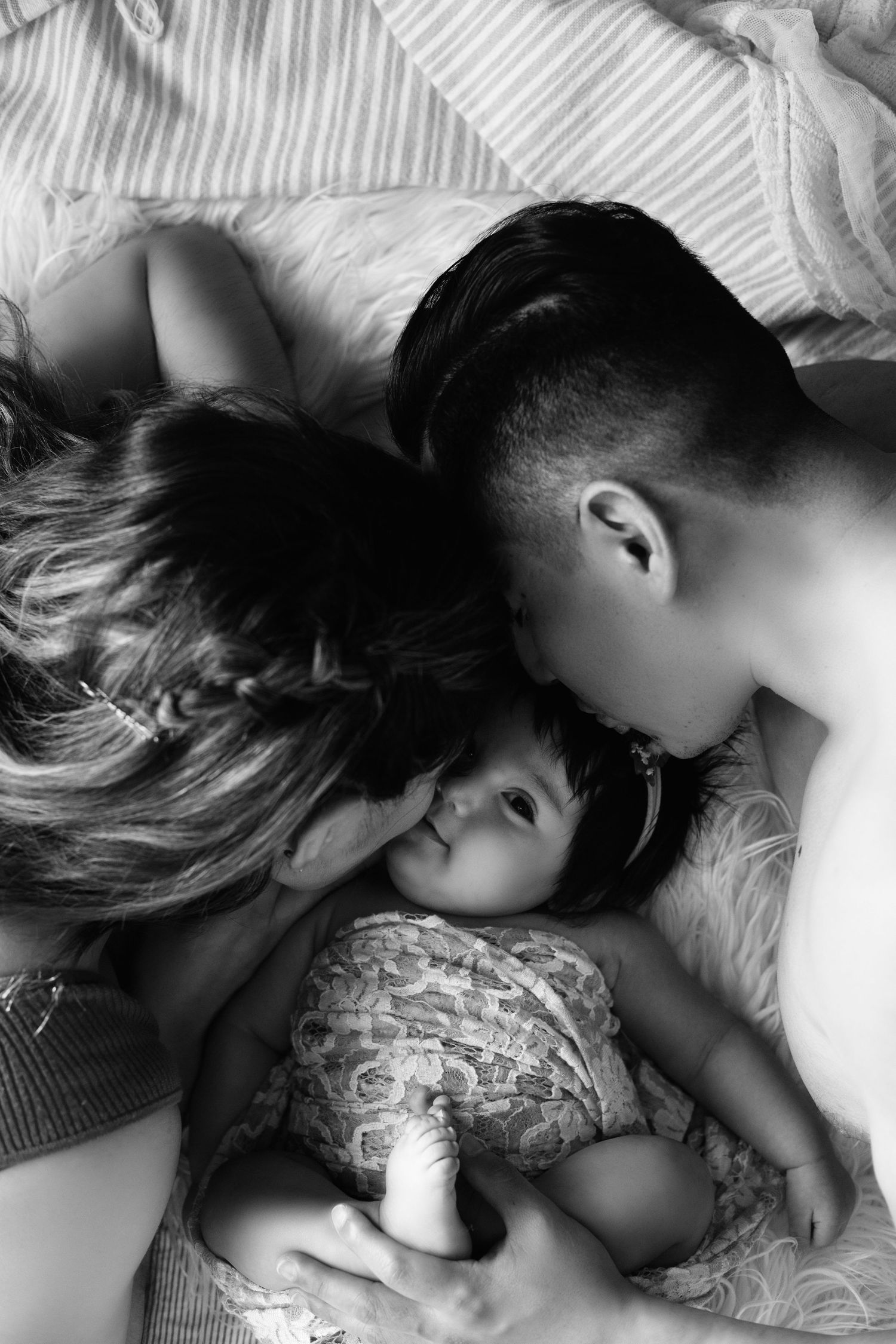 Black and white intimate portrait series showing tender family moments on white bedding.
