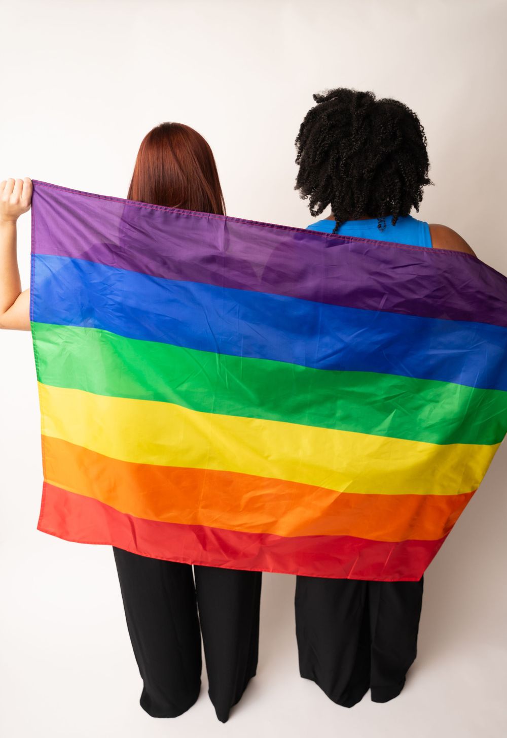 People holding rainbow pride flag against white backdrop in solidarity.