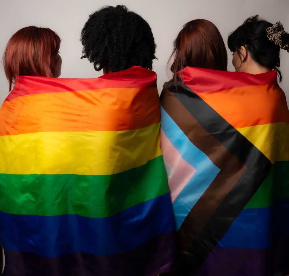 A group of people stand together while draped in rainbow Pride and transgender flags.