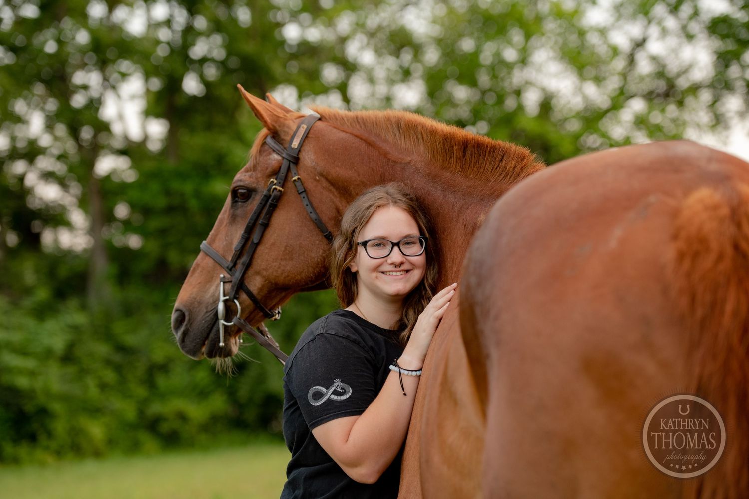 A close-up portrait of a chestnut horse and its handler against green foliage.