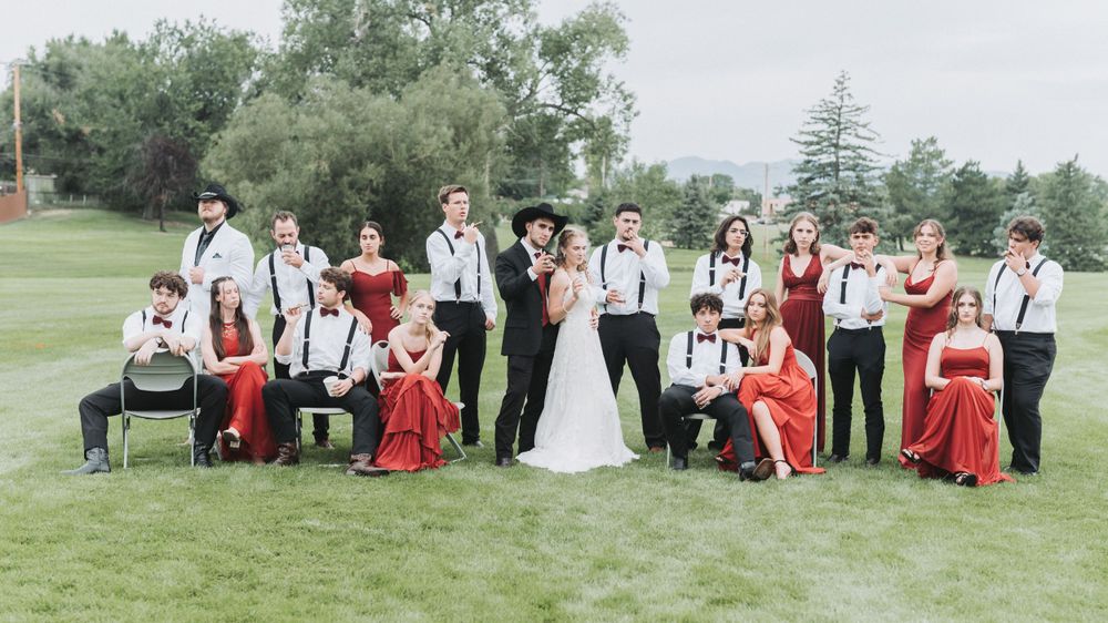 Wedding party in red and white poses on grassy lawn for group photos.