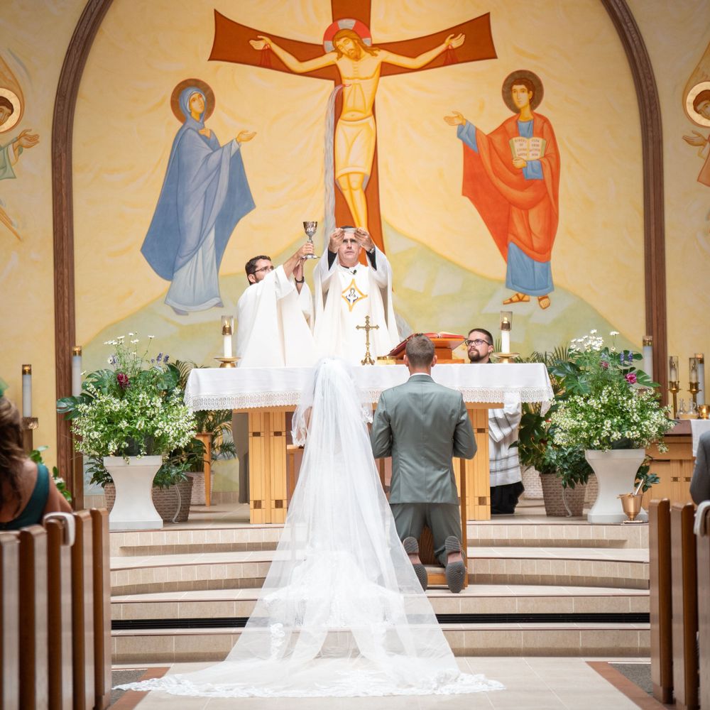A traditional church wedding ceremony with a couple kneeling at the altar beneath a crucifix.