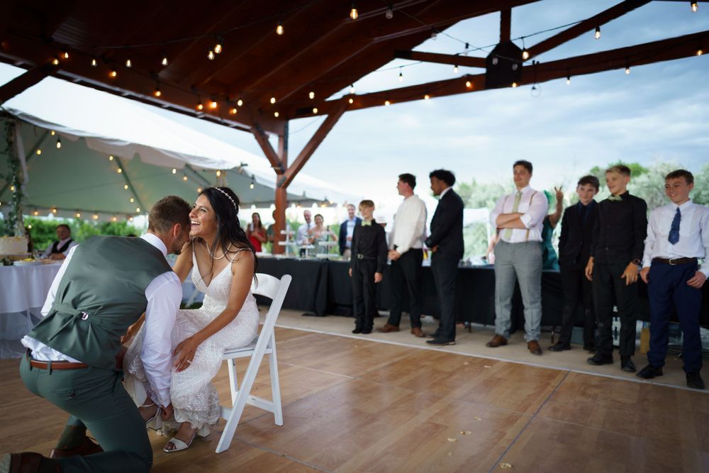 Wedding reception under covered pavilion with string lights and guests seated in white chairs.