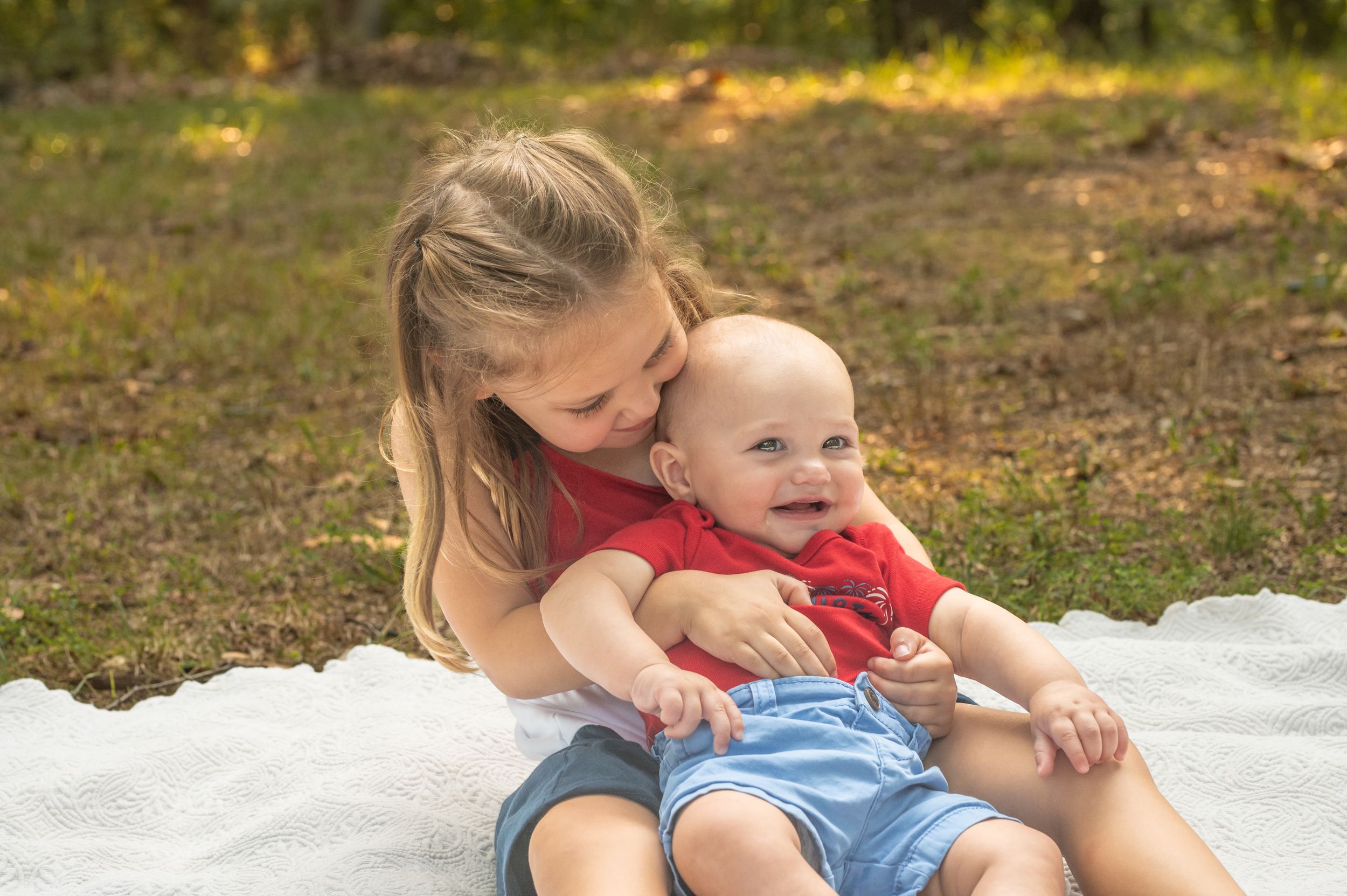 A tender outdoor moment on a blanket showing affection between child and caregiver on a sunny day.