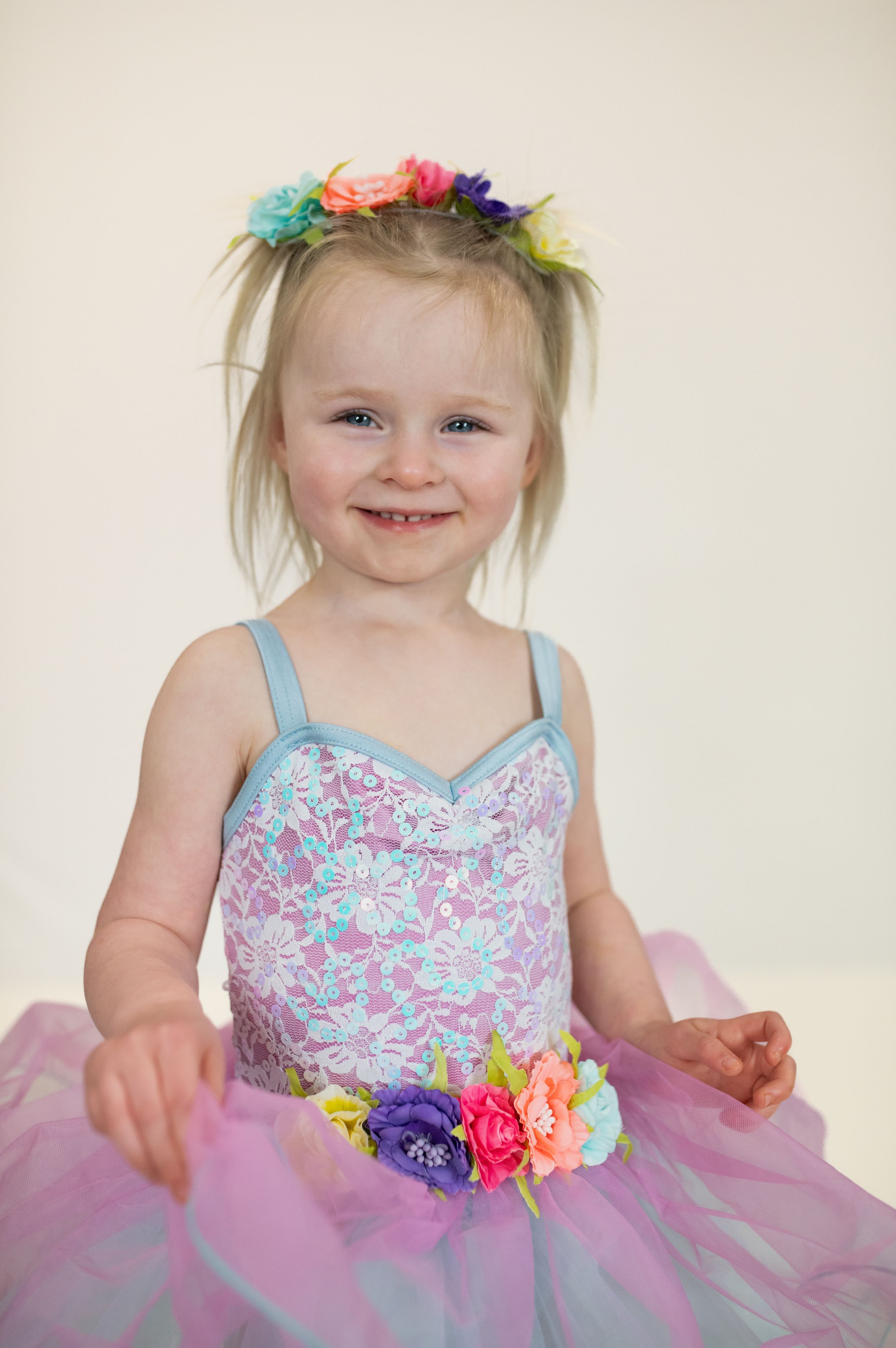 Child wearing colorful flower crown and pastel tutu dress smiling at camera.