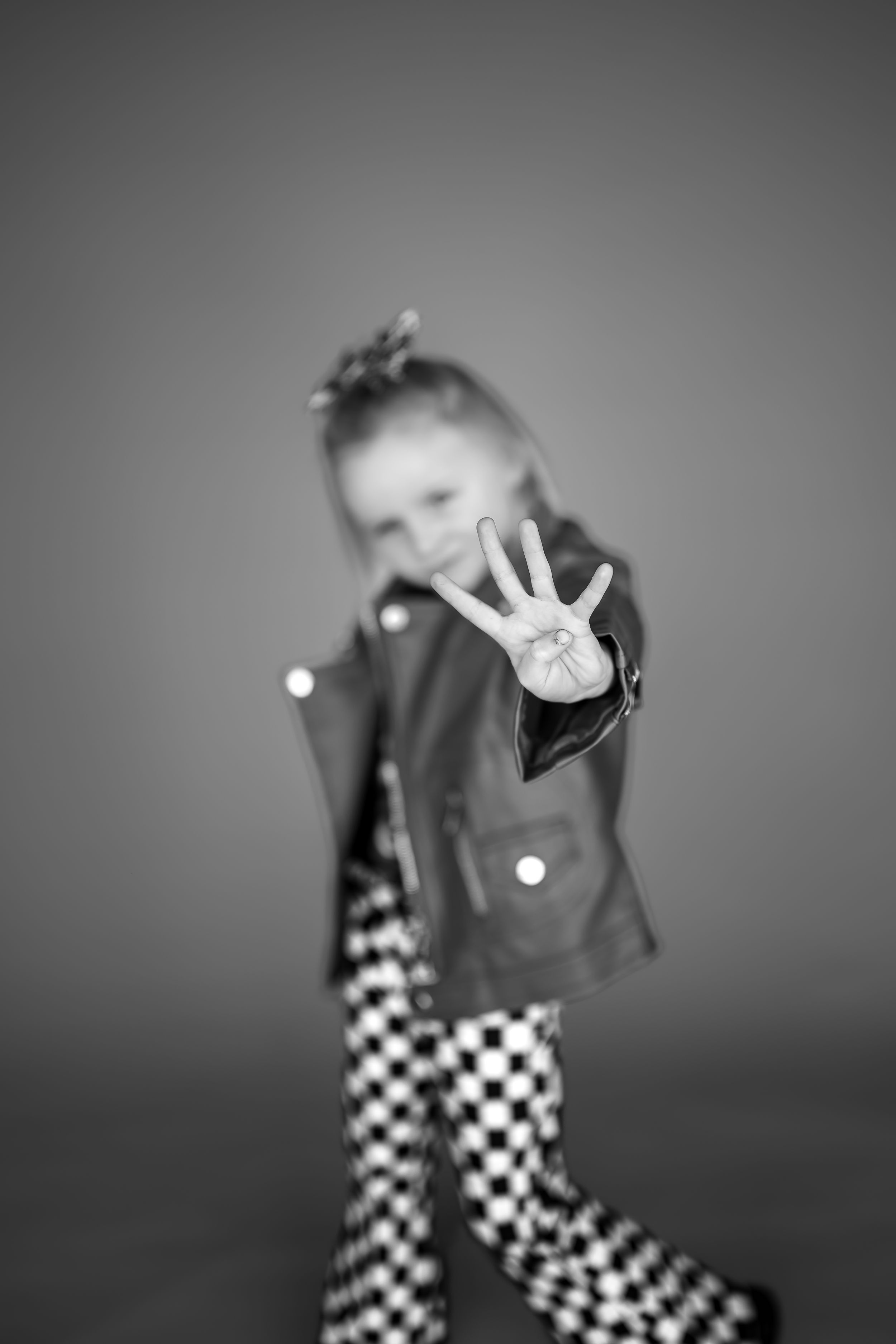 Black and white photo of a young girl in a leather jacket showing four fingers toward the camera.