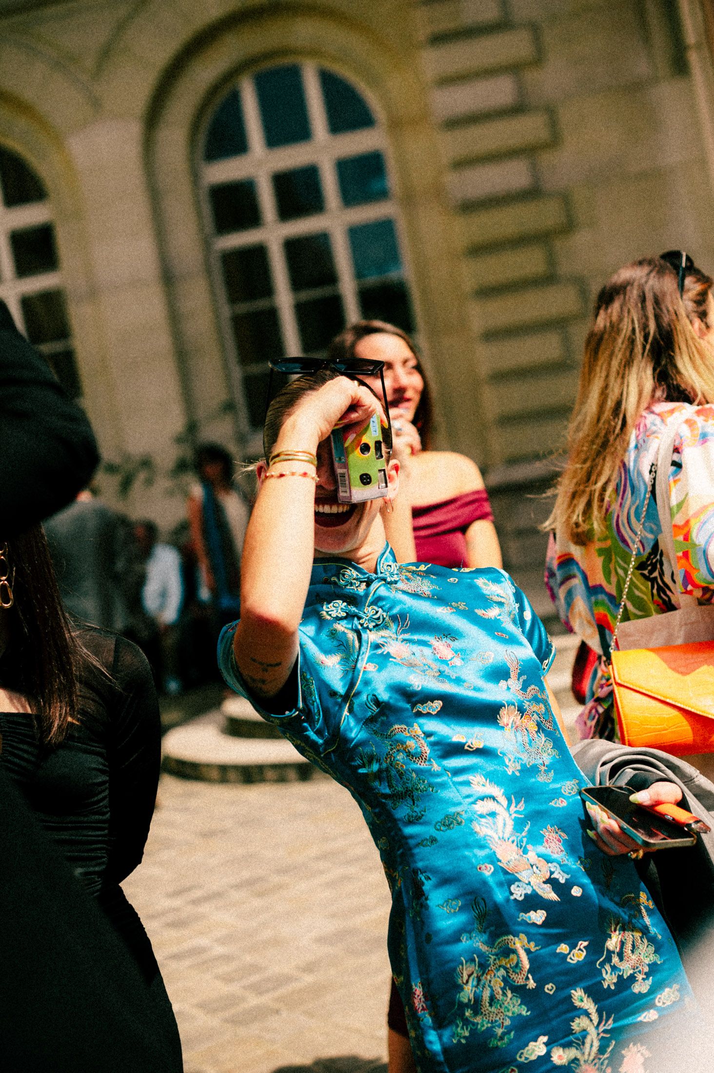 Woman in blue patterned dress dances at an outdoor social gathering near historic architecture.
