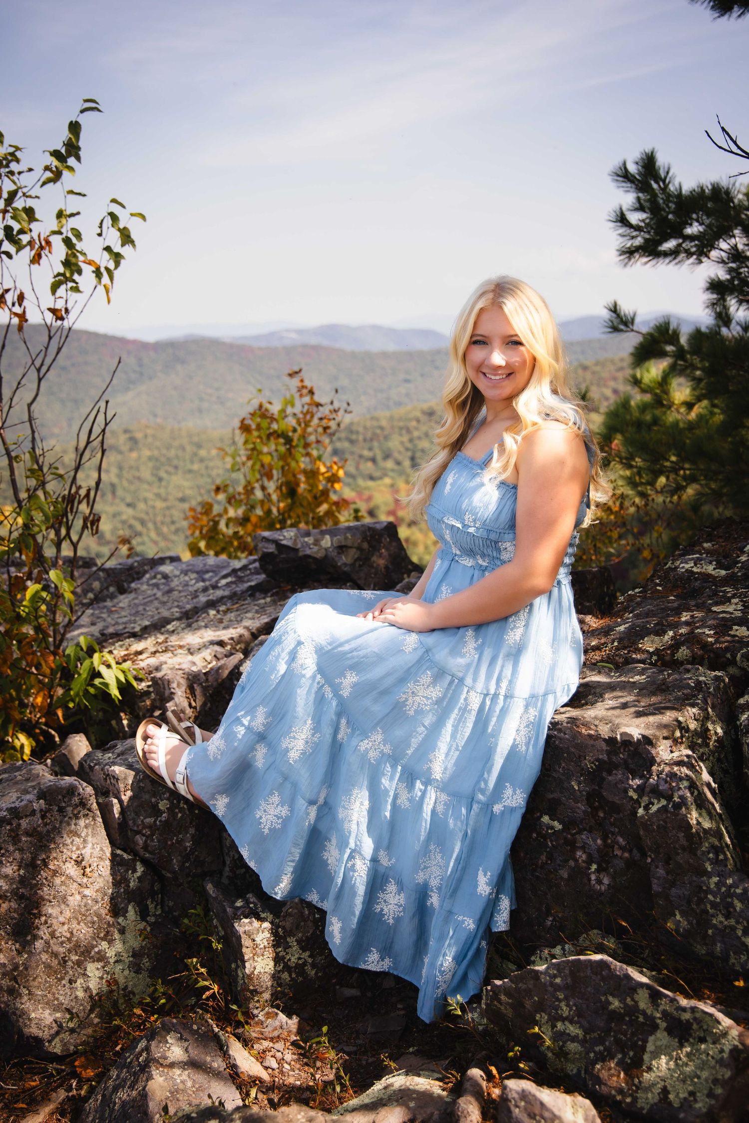 Person in a light blue dress poses elegantly on rocky mountain overlook with scenic valley views.