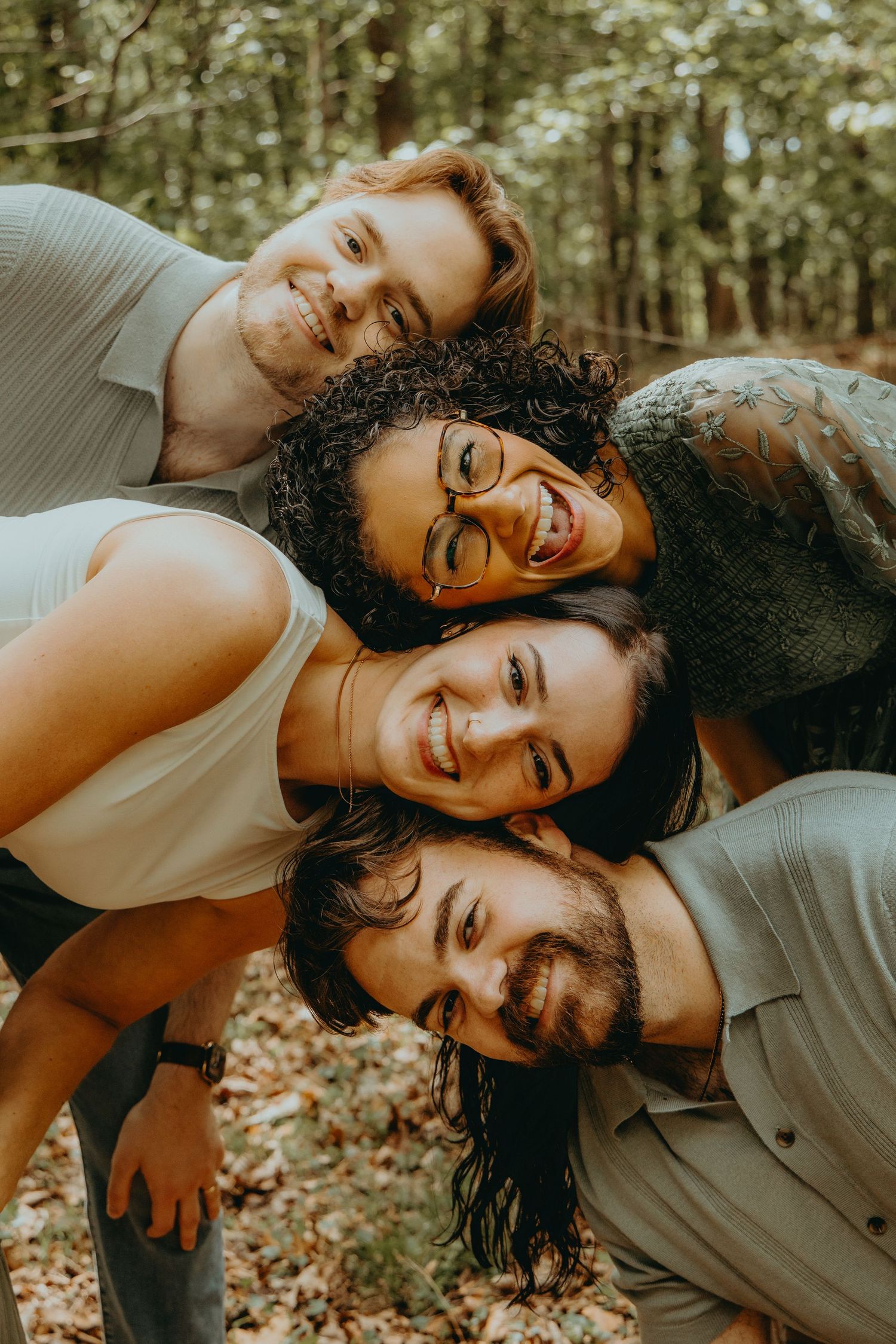 Four happy friends huddle together smiling in a forest, creating a fun stacked portrait outdoors.