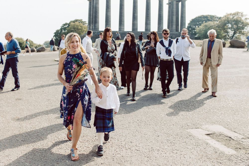 Wedding guests gather on a scenic overlook with columns and city views.