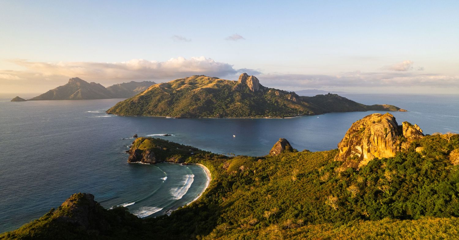 Scenic coastal landscape showing a curved bay surrounded by rugged mountains at sunset.