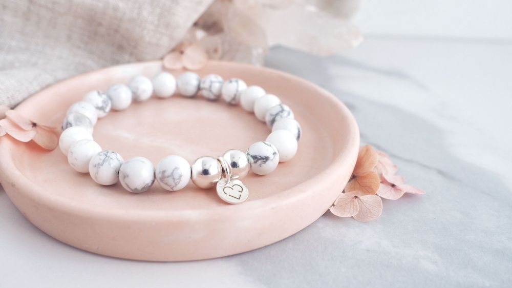 White marble beaded bracelet with silver accents displayed on pink ceramic dish.