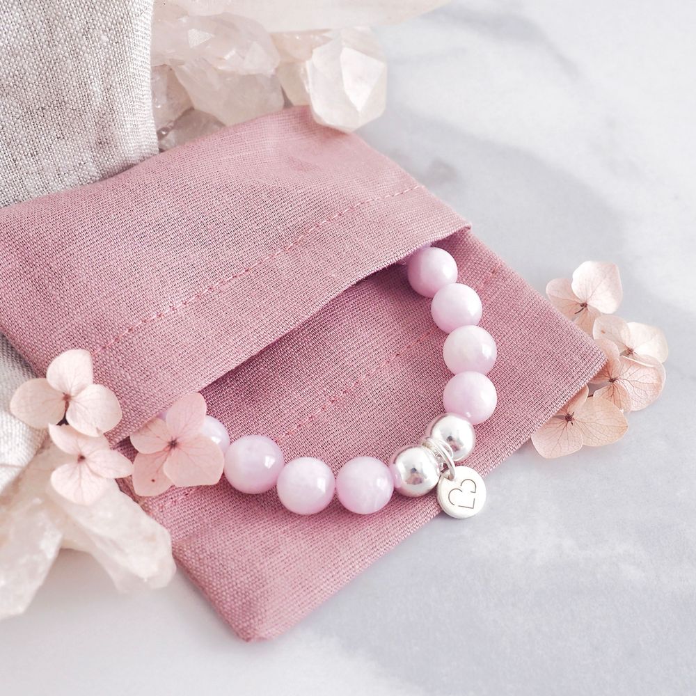 Pink beaded bracelet displayed on dusty rose linen pouch with soft lighting.