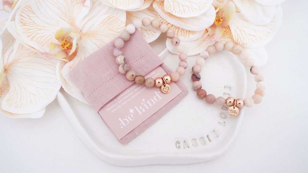 Elegant rose quartz bracelets arranged on pink pouch with white orchid flowers.