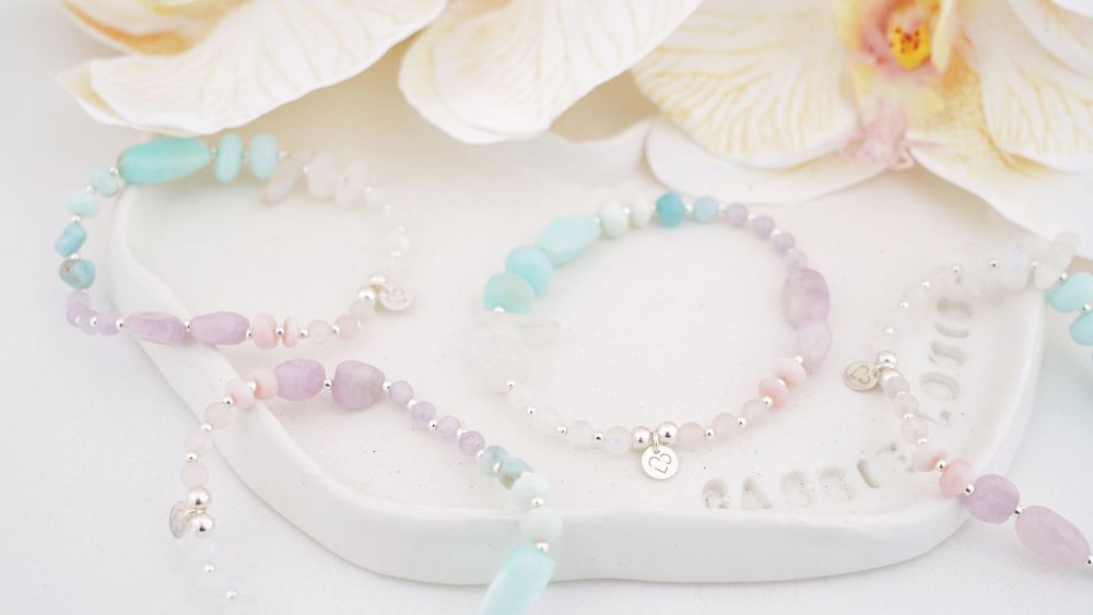 Delicate pastel and crystal beaded bracelets arranged with white orchid blooms.