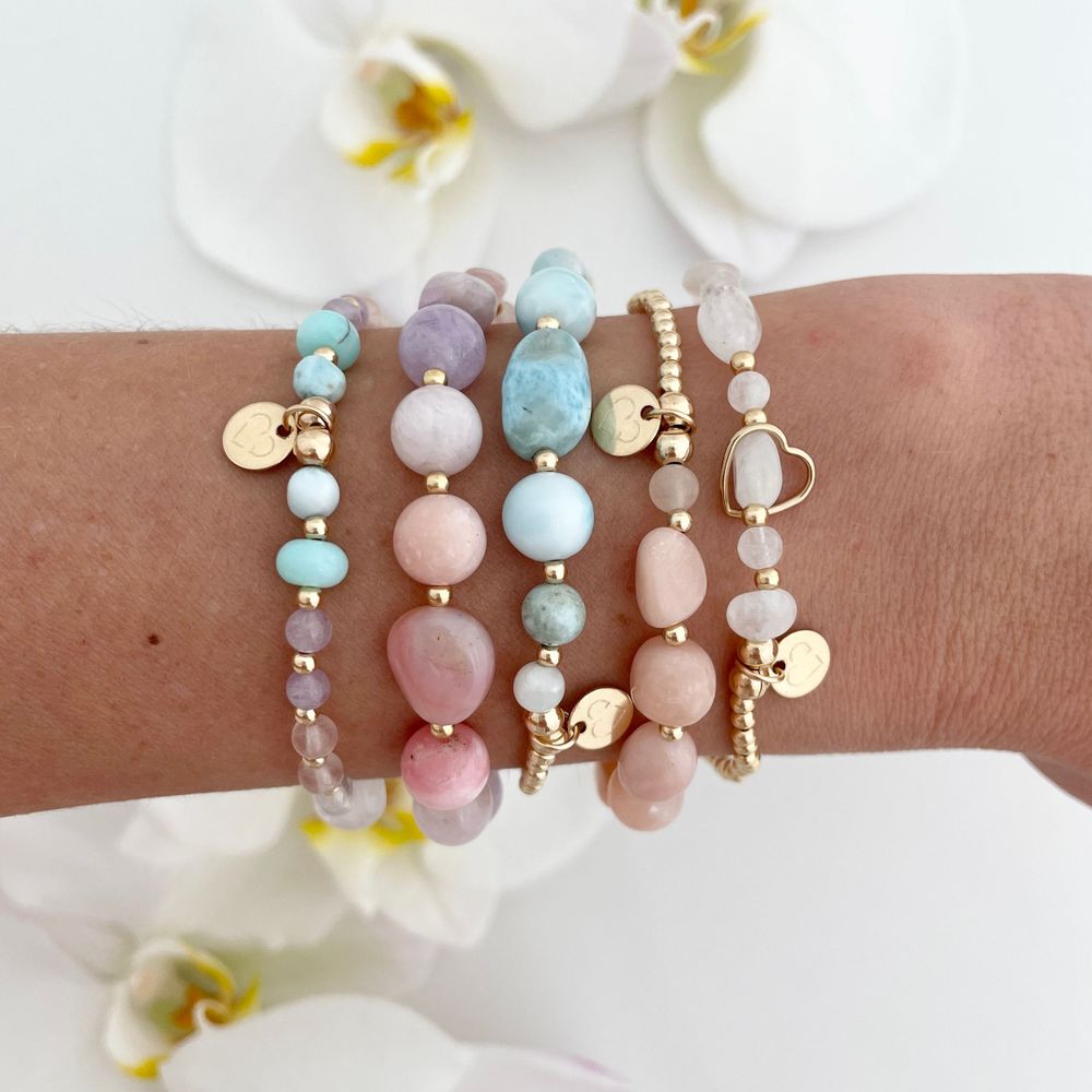 Delicate pastel beaded bracelets with gold charms displayed with orchid flowers.