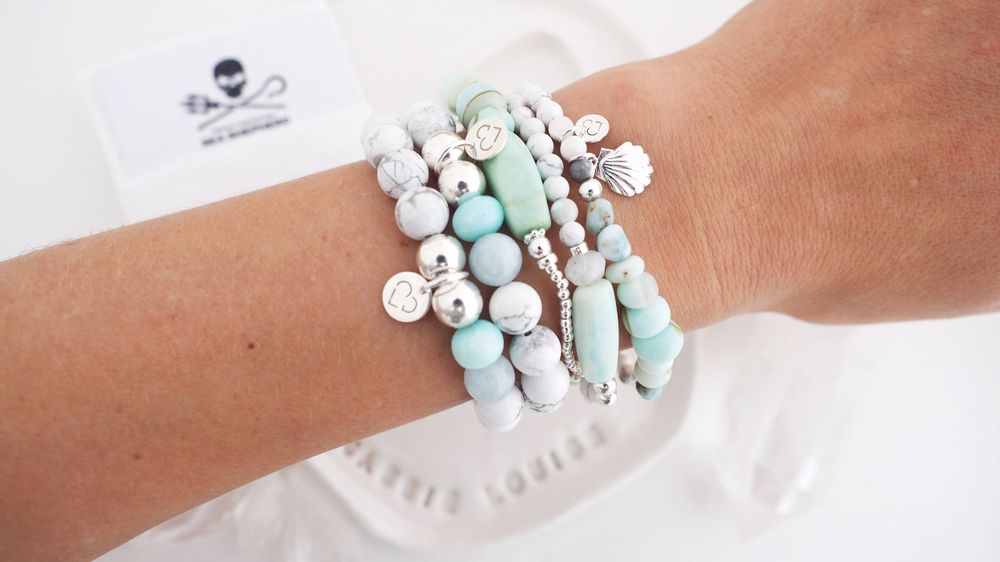 Layered stack of white and turquoise beaded bracelets worn on wrist.