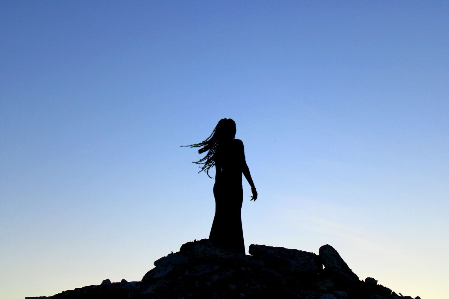 silhouette of a woman standing on a pile of rubble backlit by the blue sky