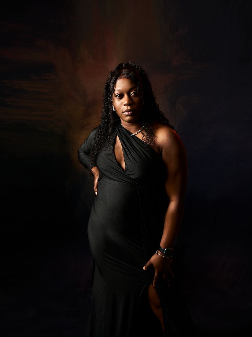 Moody maternity portraits with dramatic lighting highlighting the pregnant form in black dress.