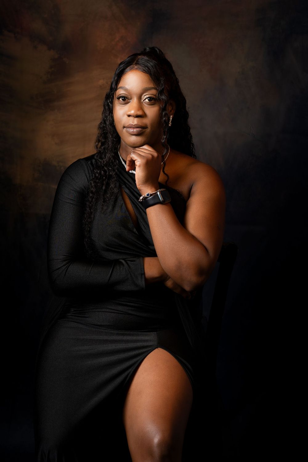 Elegant portrait of model in asymmetrical black dress against moody dark backdrop.