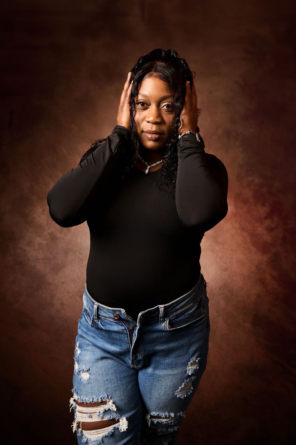 Casual maternity photos featuring distressed denim jeans and black top against warm brown backdrop.